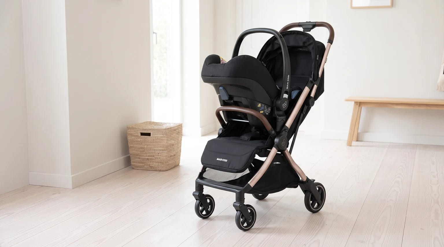 Carrinho de bebê Maxi-Cosi Eva³ preto, com estrutura rosé e bebê-conforto acoplado, na entrada iluminada de uma casa.
