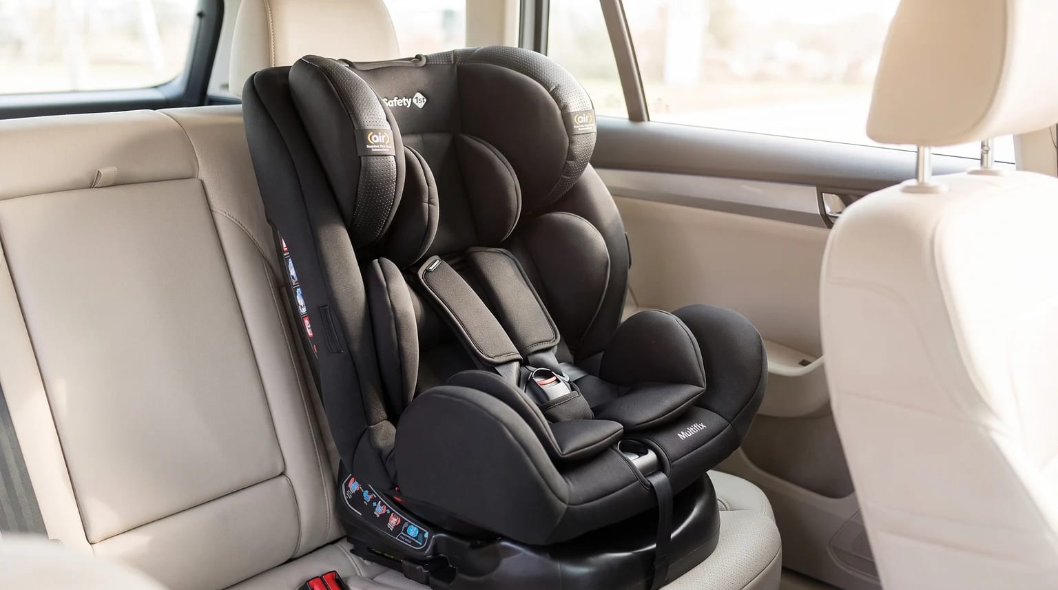 Cadeirinha Safety 1st Multifix preta posicionada no banco traseiro de um carro com estofado claro.
