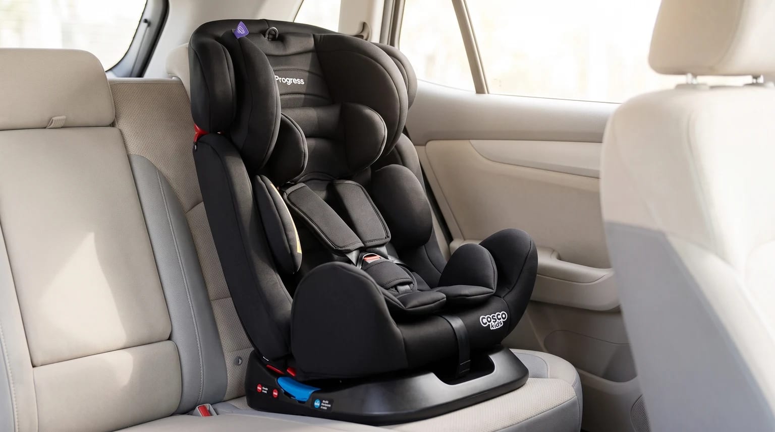 Cadeirinha Cosco Progress preta posicionada no banco traseiro de um carro com estofado claro.