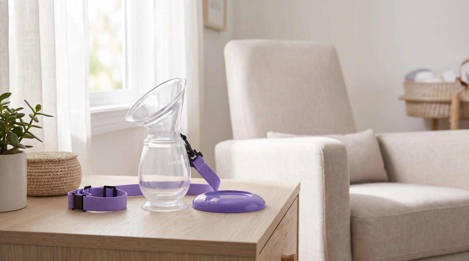Coletor de silicone Lansinoh com cordão e base roxa sobre uma mesa de madeira clara, com uma poltrona ao fundo.