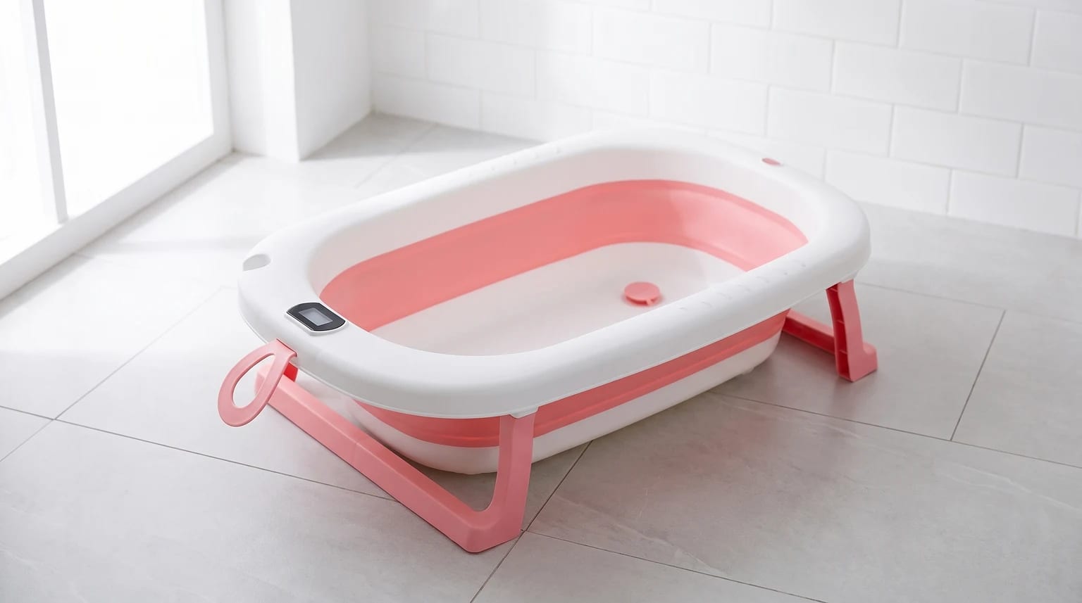 Banheira de bebê dobrável branca e rosa, com termômetro digital, montada no chão de um banheiro.