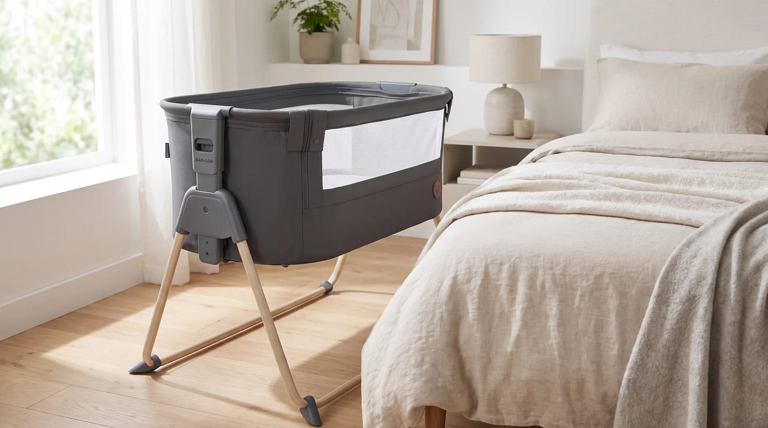 Berço Maxi-Cosi Tori cinza com estrutura de efeito amadeirado, ao lado de uma cama.