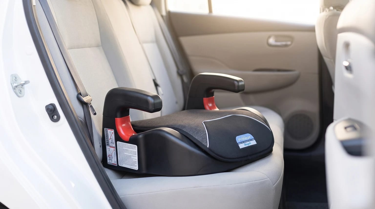 Assento de elevação Burigotto Protege sem encosto, preto e cinza, no banco traseiro de um carro com interior claro.