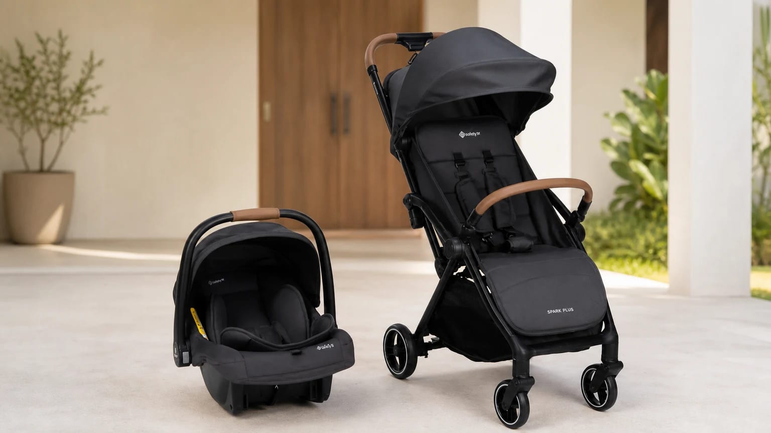 Carrinho Safety 1st Spark Plus preto e bebê-conforto ao lado, apoiados no piso de uma entrada residencial.