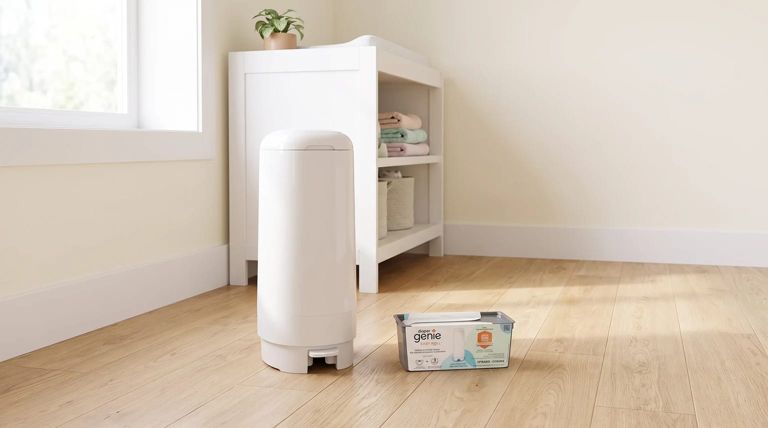 Lixeira Diaper Genie branca ao lado de um trocador, com um refil Easy Roll no chão.