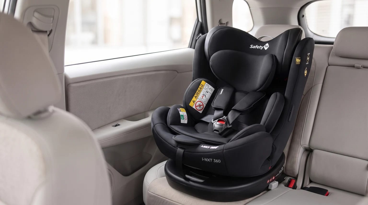 Cadeirinha Safety 1st i-NXT 360 preta posicionada no banco traseiro de um carro com interior claro.
