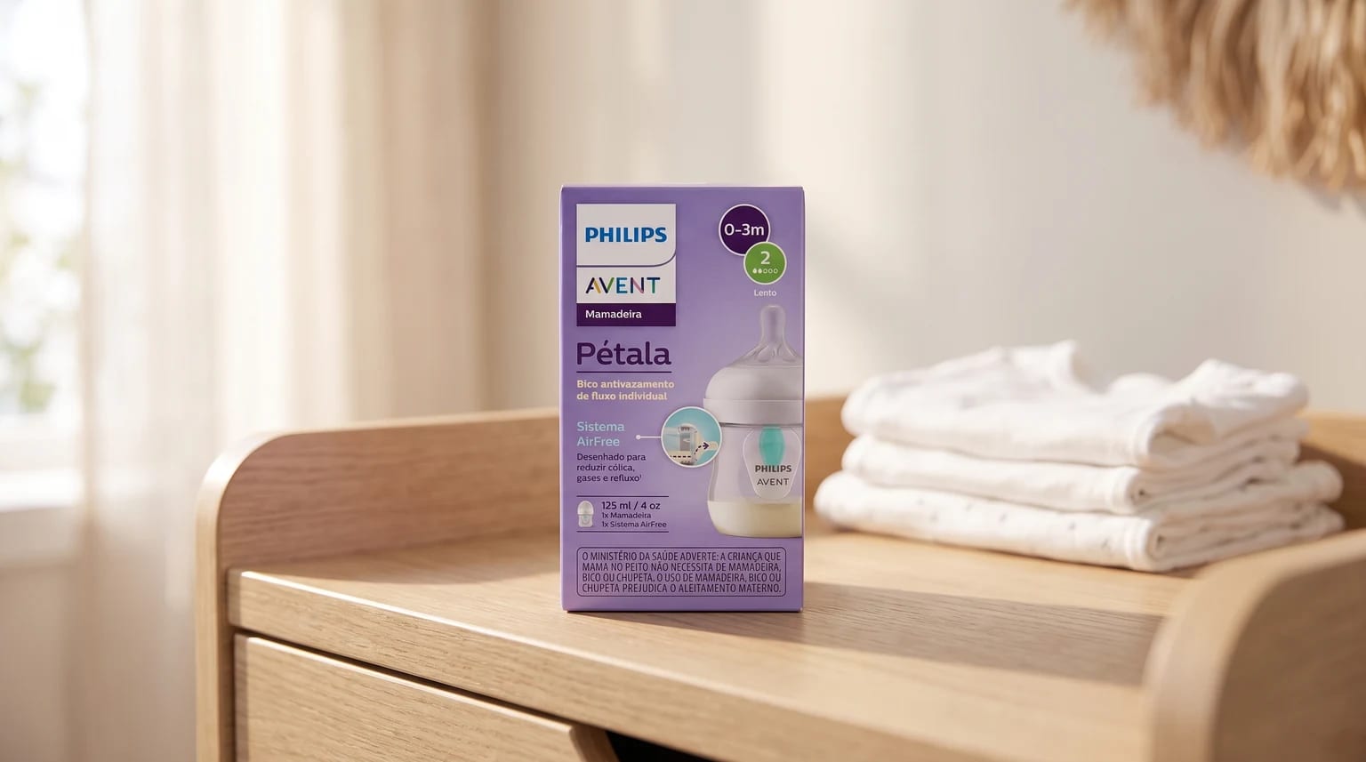 Caixa da mamadeira Philips Avent Pétala em cima de um trocador de madeira, ao lado de uma pilha de roupas de bebê brancas.