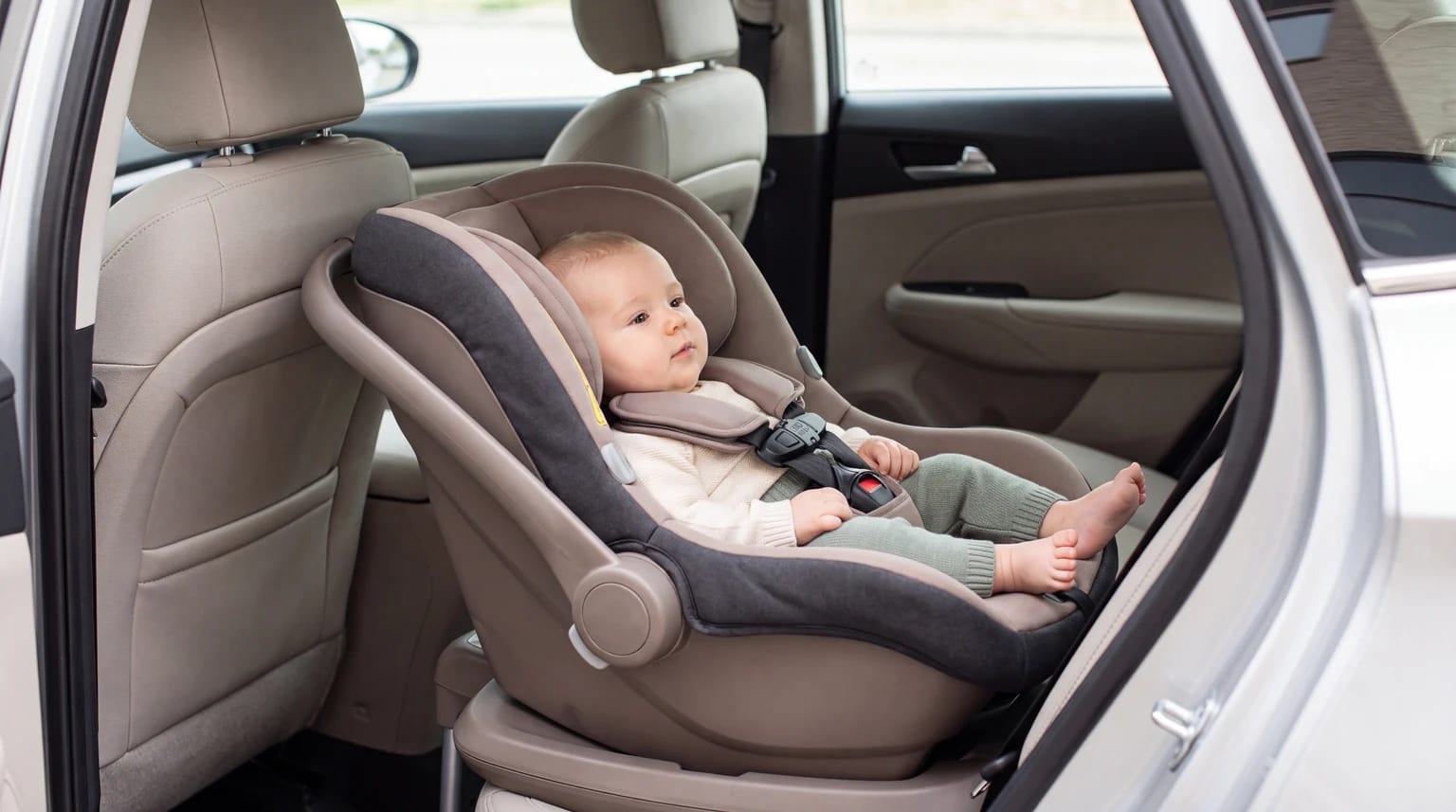 Bebê pequeno em uma cadeirinha virada para trás, visto pela porta traseira aberta de um carro.