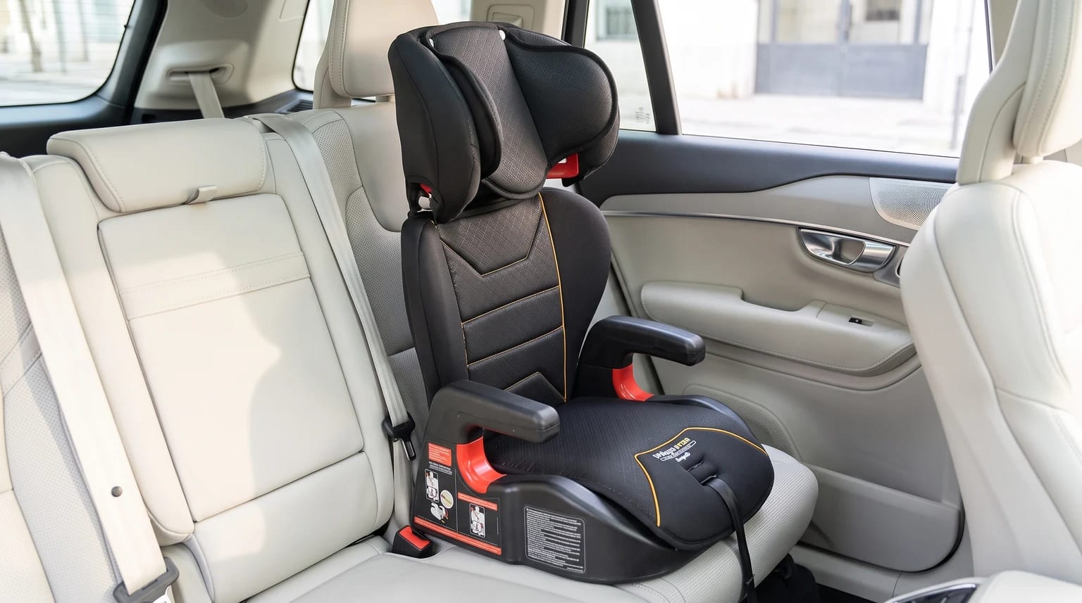 Assento de elevação Burigotto Protege Fix com encosto, preto com costura amarela, no banco traseiro de um carro com interior claro.