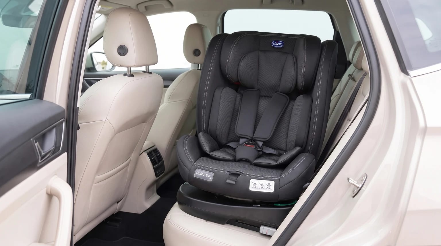 Cadeirinha Chicco Unico Evo i-Size preta posicionada no banco traseiro de um carro com interior bege.