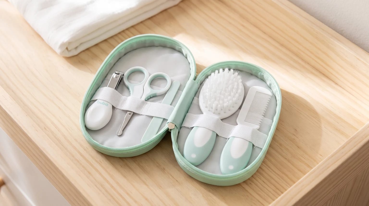 Kit de higiene para bebê em estojo verde-claro aberto sobre uma superfície de madeira, com escova, pente, tesoura, cortador e lixa de unha.