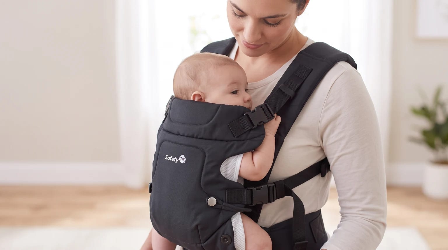 Mãe olha para um bebê acordado em um canguru preto da Safety 1st, em uma sala clara.