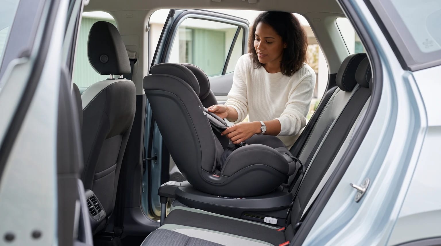 Mãe gira uma cadeirinha 360° vazia em direção à porta traseira aberta do carro.