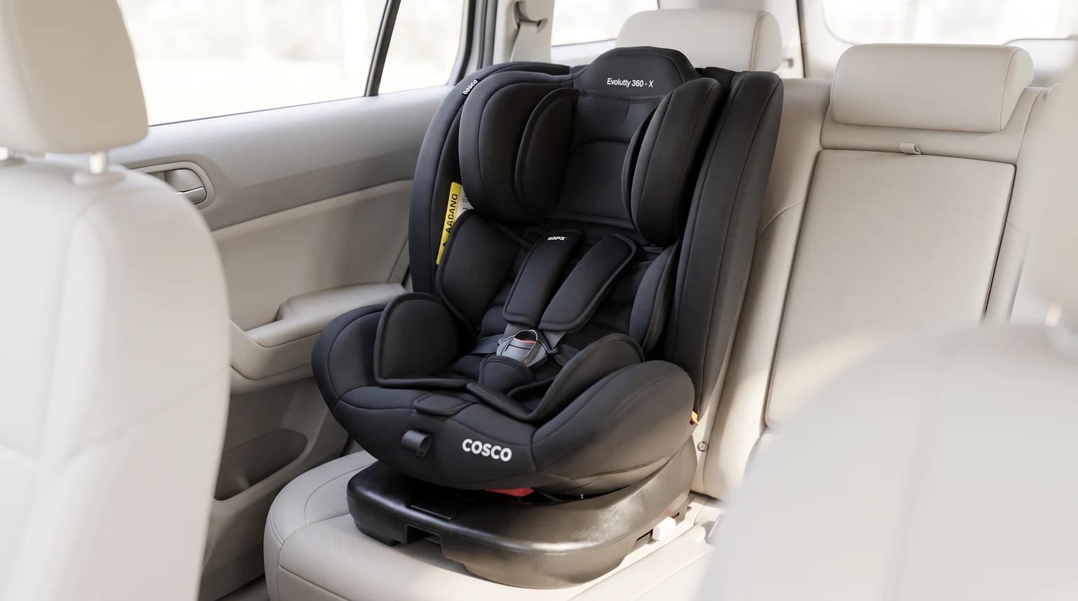 Cadeirinha Cosco Evolutty 360 X preta posicionada no banco traseiro de um carro com interior claro.