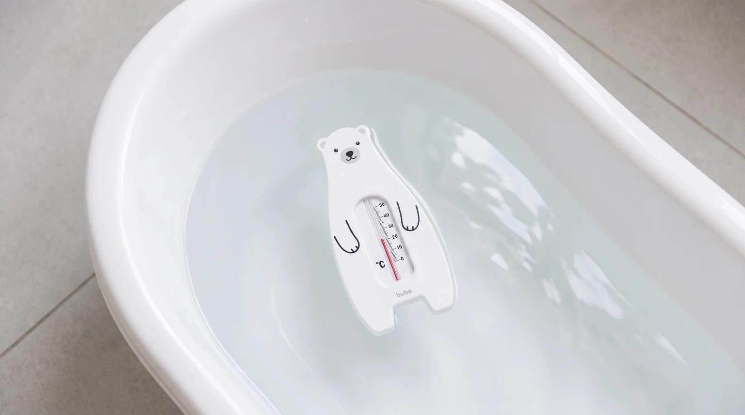 Termômetro branco em formato de urso sobre a água de uma banheira de bebê.