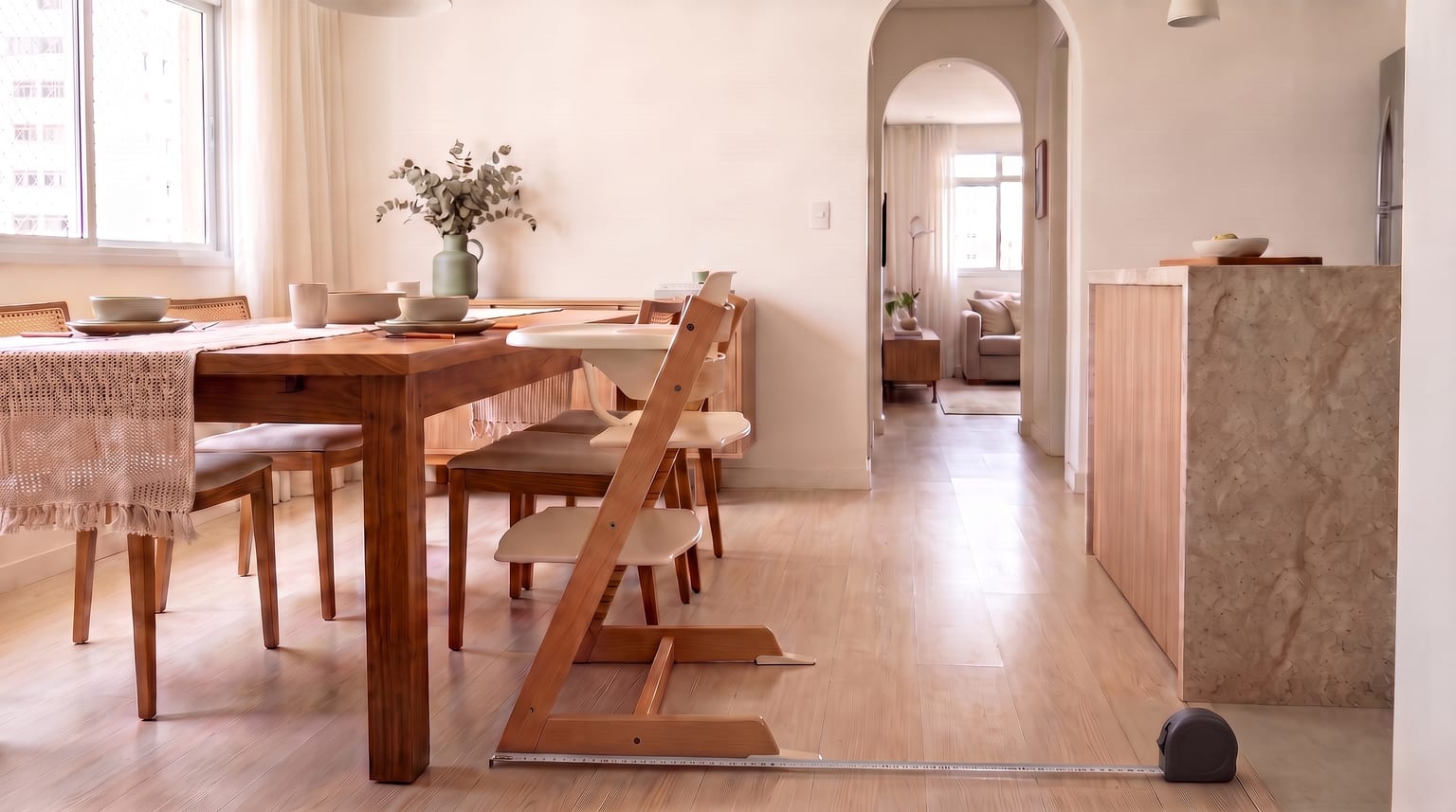 Cadeira de alimentação de madeira ao lado de uma mesa de jantar, com uma trena retrátil estendida no chão ao longo de sua base.